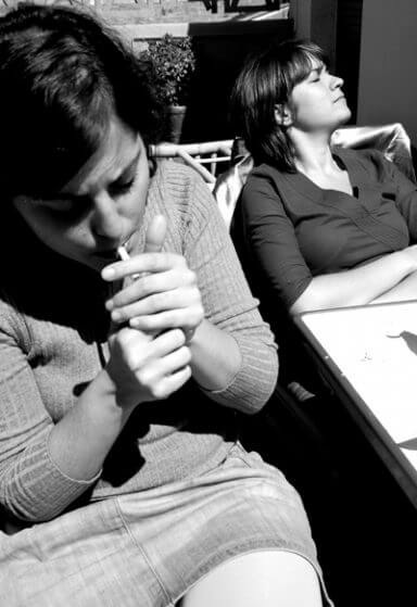A woman smokes while her coaddict loved one ignores it in the background