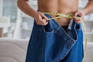 A man wearing loose pair of jeans with a yellow tape measure wrapped around his waist 