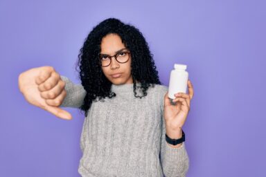A woman holding a white drug bottle doing a thumbs down sign