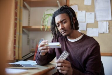 A man in his room reading the box of a drug packaging