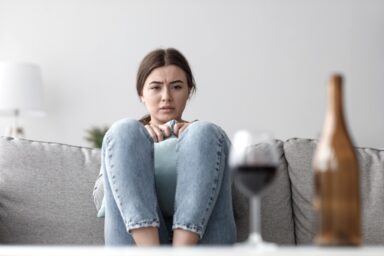 Woman sitting on the couch staring a wine glass and bottle
