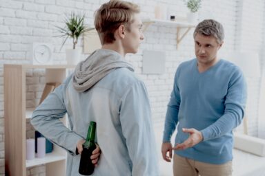 Teenage boy hiding an alcohol bottle from his father