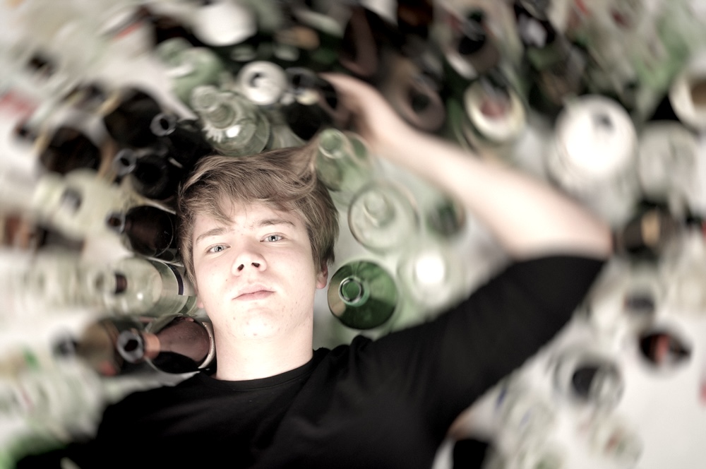 Teenage boy lying down on the ground surrounded by empty alcohol bottles