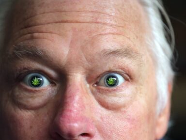 Closeup of a man’s face with widely opened eyes mirroring marijuana leaves