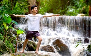 A young man practicing yoga meditation and breathwork in forest near waterfall.