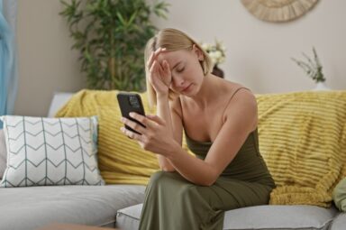 Young blonde woman who lost a loved one sitting on a couch reading a comforting text message 