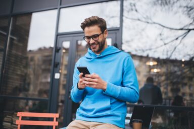 Man in a blue hoodie reading quotes on his phone outside a cafe